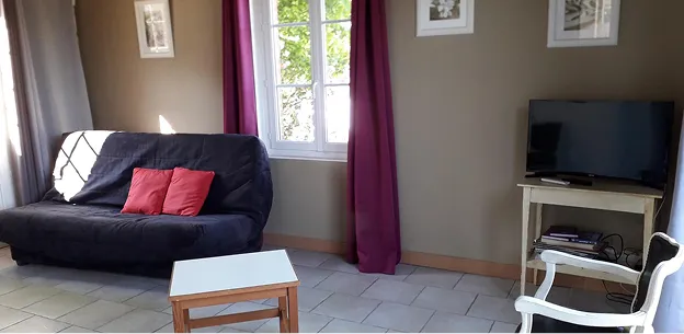 Salon chaleureux avec canapé-lit noir, coussins rouges, table basse, TV et fenêtre lumineuse à Autrèche près de Tours et d'Amboise en Indre-et-Loire 37